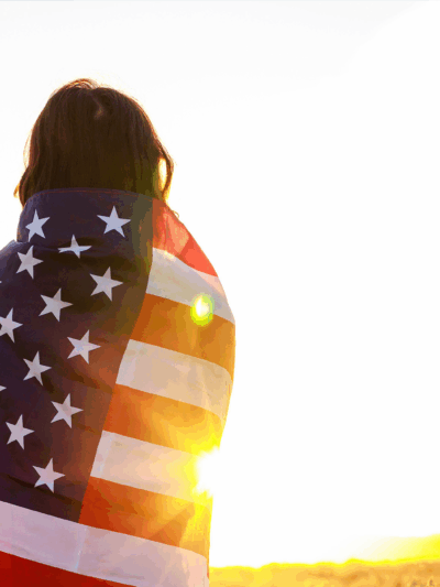 Woman in field holding USA stars and stripes flag in golden sunset evening sunshine