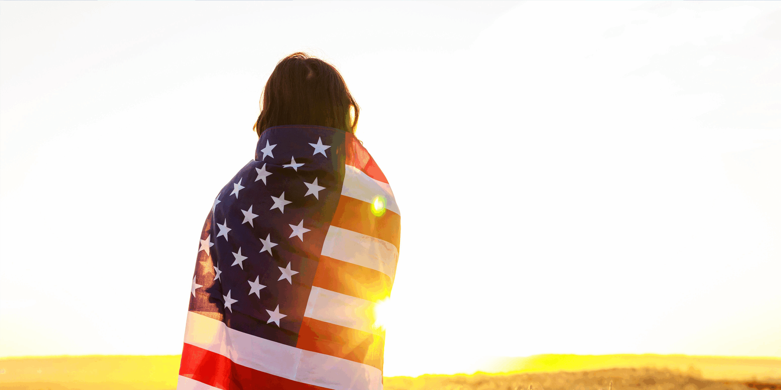 Woman in field holding USA stars and stripes flag in golden sunset evening sunshine