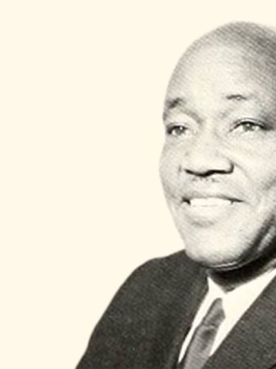 A black and white photo of Dr. Ezra Totton, a Black man, wearing a suit and smiling in a headshot picture with a cream-colored background.