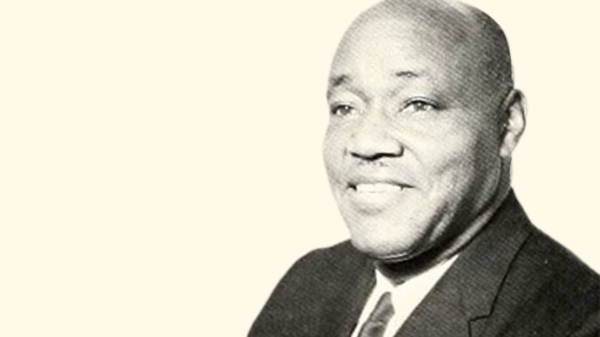 A black and white photo of Dr. Ezra Totton, a Black man, wearing a suit and smiling in a headshot picture with a cream-colored background.