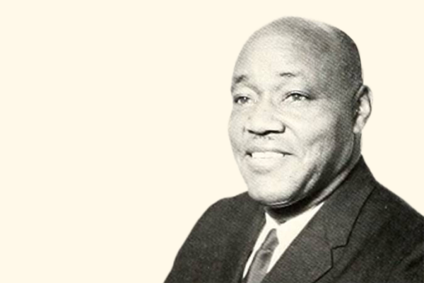 A black and white photo of Dr. Ezra Totton, a Black man, wearing a suit and smiling in a headshot picture with a cream-colored background.